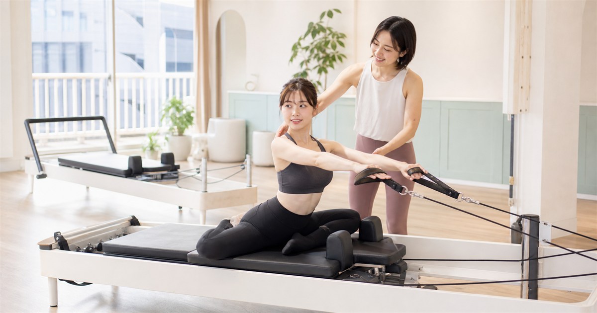明るいマシンピラティススタジオでインストラクターの指導を受ける女性